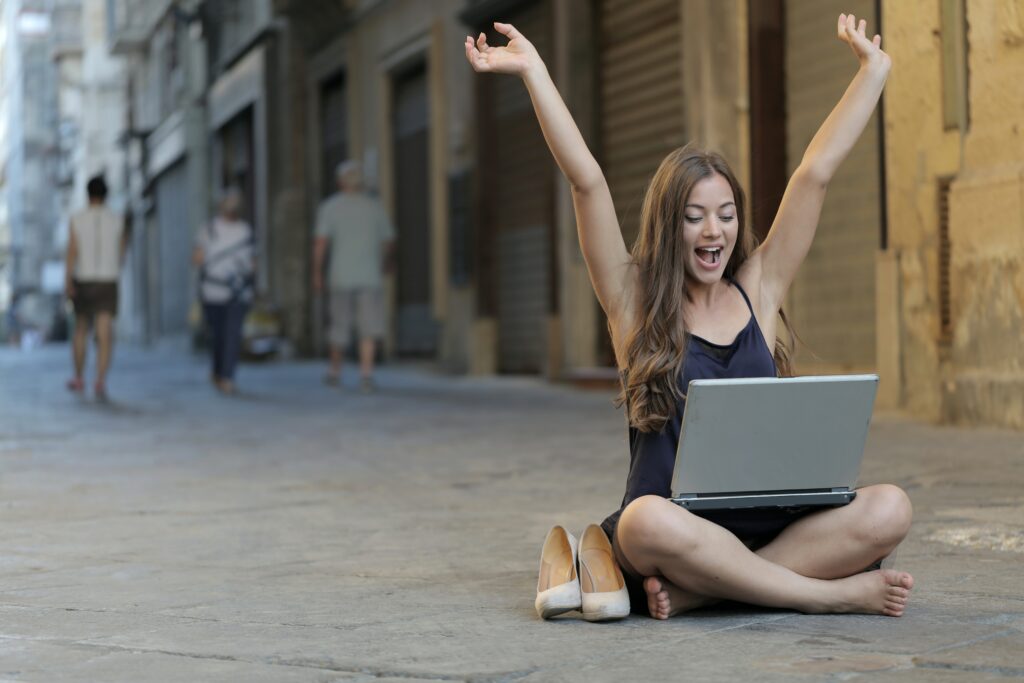 Mulher sentada na rua com um laptop a celebrar por ter saído da sua zona de conforto.