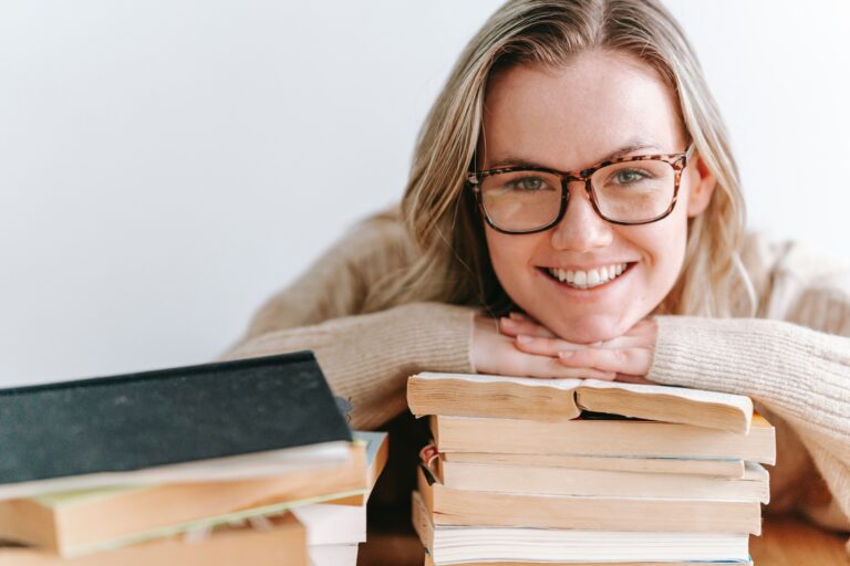 Jovem mulher com o rosto apoiado em cima de uma pilha de livros sorri por ter conseguido vencer a procrastinação.