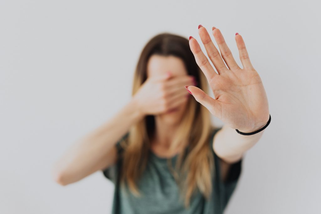 Mulher tapa a cara com uma mão e com a outra faz um sinal de parar, manifestando medo, uma das 5 emoções básicas.