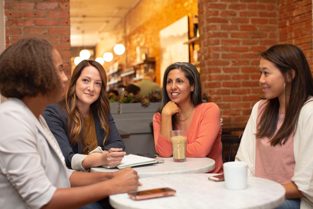 Mulheres sentadas à mesa aplicam táticas de negociação numa conversa de trabalho.