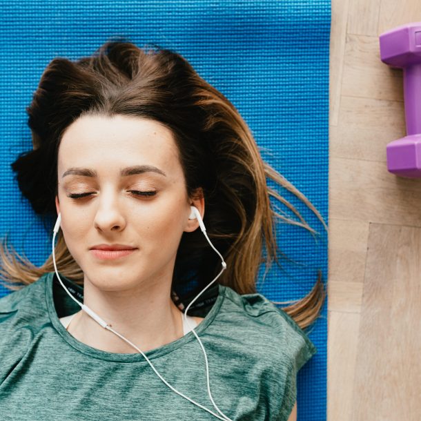Jovem mulher deitada num tapete de yoga, com headphones nos ouvidos põe em prática técnicas de relaxamento como a meditação e o mindfulness.
